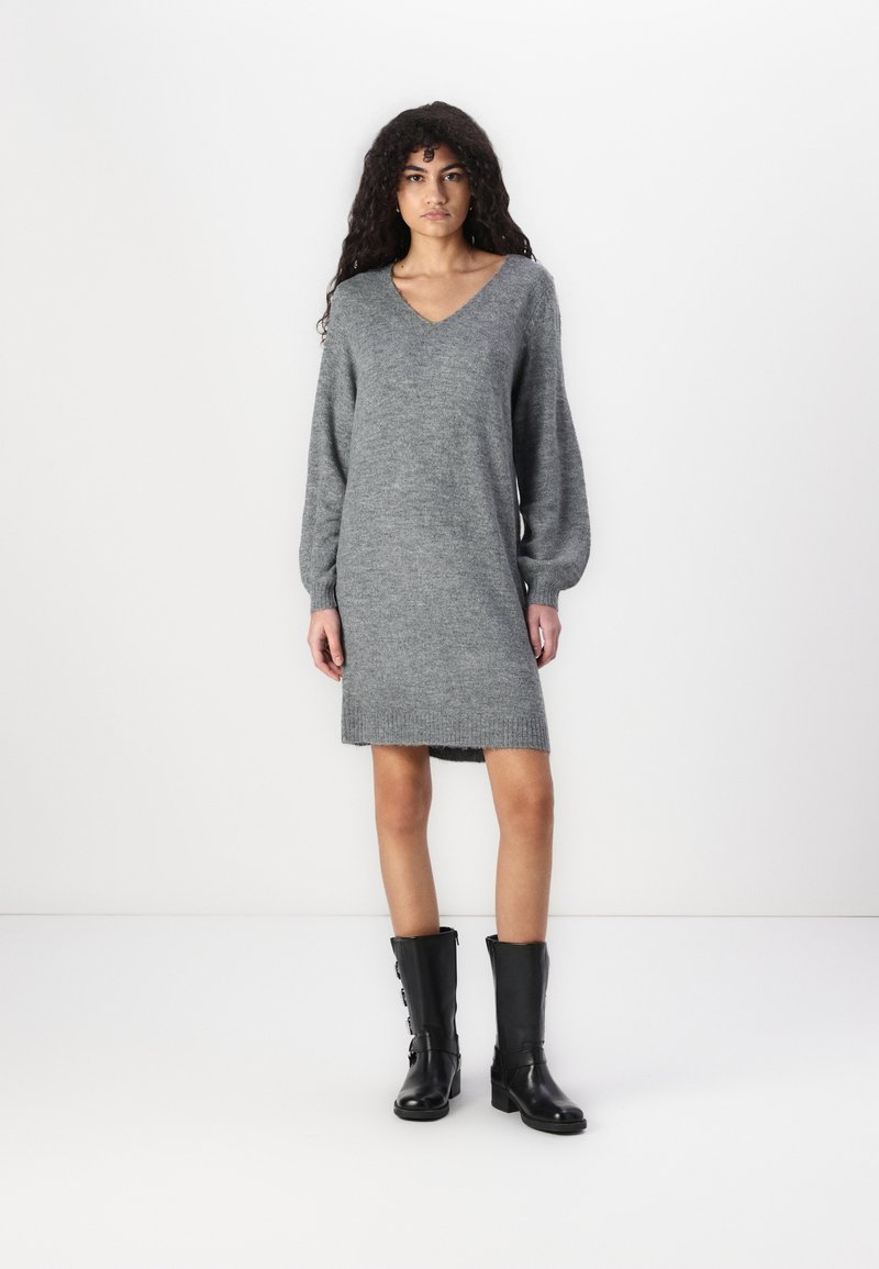 Robe en tricot grise avec un décolleté en V, des manches longues et un ourlet côtelé, associée à des bottes en cuir noires jusqu'au genou avec des zips latéraux.