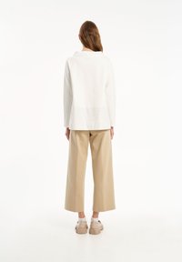 Camicia bianca dal taglio morbido con yoke posteriore e orlo spaccato, abbinata a pantaloni beige a gamba larga e sneakers beige.