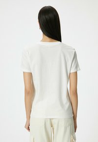 Hvid t-shirt med korte ærmer, rund halsudskæring, lavet af glat bomuldsstof. Bagfra ses rene linjer og et enkelt design uden udsmykninger.