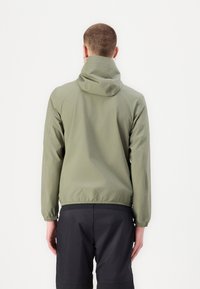 Lättviktig, olivgrön jacka med huva, elastiska muddar och dragsko i nederkant. Kombinerad med svarta shorts, sedd från baksidan.