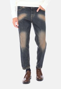 Jeans in denim scuro con toppe sbiadite, cinque tasche e vestibilità ampia. Abbinati a scarpe in pelle marrone con una suola spessa e testurizzata.