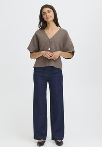 Brun, V-ringad blus med knappar och vida ärmar, tillsammans med mörkblå högmidjade jeans. Mjuk textur, avslappnad design.