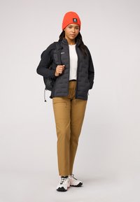 Vadderad svart jacka, vit skjorta, beige byxor, orange mössa och vita sneakers med svarta och orange detaljer. Justerbara remmar på jackan.