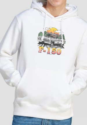 Person trägt einen weißen Hoodie mit einem bunten Vintage-Lastwagen-Motiv und dem Schriftzug "F-150" auf der Vorderseite, kombiniert mit blauen Jeans.