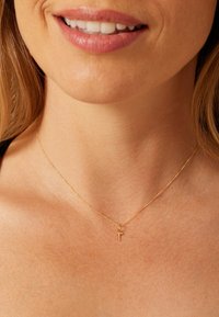 Gold necklace with a delicate chain and small cross pendant, resting on bare skin. Smooth texture, fine links, and subtle shine.