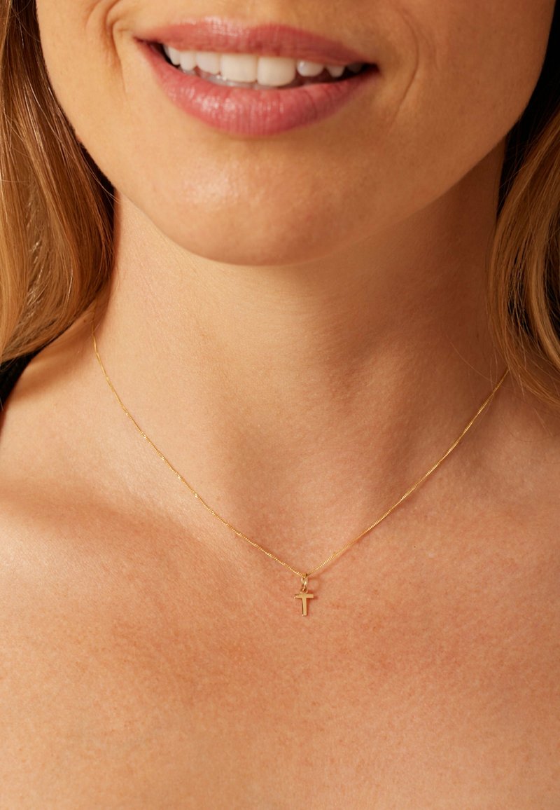 Gold necklace with a delicate chain and small cross pendant, resting on bare skin. Smooth texture, fine links, and subtle shine.