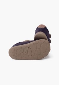 Dark blue suede shoe with a brown accented toe. Features velcro straps and a textured brown rubber sole with rounded shapes and "Made in Spain" inscription.