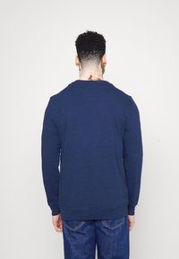 Navy blue long-sleeve sweatshirt with ribbed cuffs and hem, made of textured fabric. Viewed from the back, worn with blue jeans.