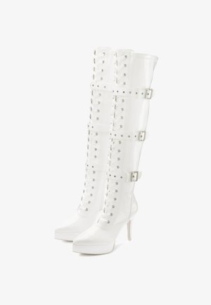 White patent leather knee-high boots with a pointed toe, lace-up front, and three buckle straps; features a high stiletto heel and platform sole.