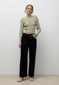 Heled rohelise soonikuga kardigan, millel on pikad varrukad ja ees nööbid, on paaritatud kõrge talje ja laiad mustad püksid ning heledate kollaste kontsadega.