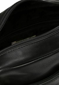 Interior de bolsa de cuero negro con un bolsillo con cremallera, que presenta una textura suave y detalles de costura a lo largo de las costuras.