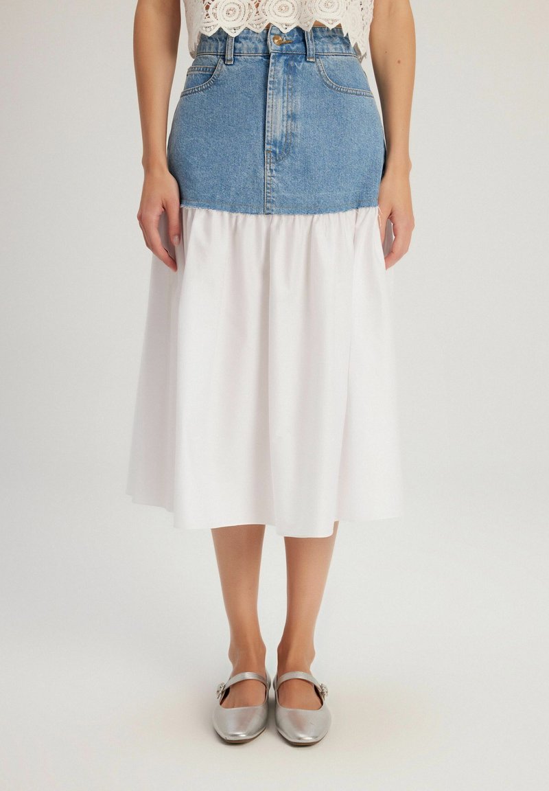 Jupe en denim et blanche, ajustée à la taille avec une partie inférieure évasée blanche. La jupe présente un design bicolore et cinq passants de ceinture.