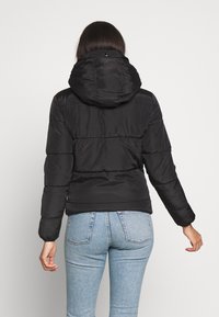 Doudoune noire avec capuche, présentant un motif matelassé et des poignets élastiques, associée à un jean taille haute bleu clair.