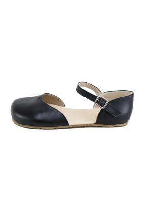 Zapato plano negro con puntera redondeada cerrada, laterales abiertos, plantilla beige y correa ajustable en el tobillo con hebilla metálica sobre fondo blanco.