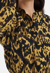 Koszula w panterkę w kolorze żółtym i czarnym, wykonana z miękkiego materiału, z zapięciem na guziki oraz kołnierzykiem z marszczeniami.