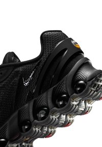 Gros plan d’une chaussure de sport noire avec une tige texturée, le Swoosh Nike visible et une semelle distinctive avec des coussins d’air.