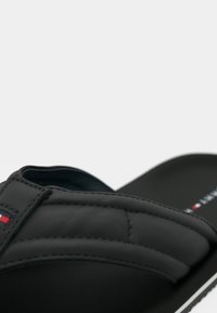 Μαύρο σανδάλι με λουρί τύπου slide και επάνω μέρος με ραφές, που φέρει λογότυπο. Απαλή υφή, μίνιμαλ σχεδιασμός και αντίθετη λευκή σόλα.