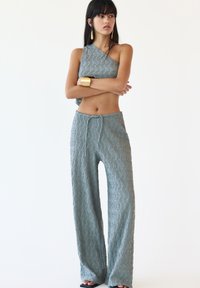 Light blue textured two-piece outfit featuring a one-shoulder top and wide-leg pants with a drawstring waist. Accents include gold earrings and bracelet.