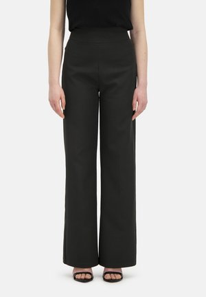 Wijdvallende broek in donkergroene stof met een hoge taille, voorzien van een zachte textuur en strakke lijnen. Gecombineerd met zwarte bandjesandalen.