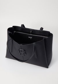 Sac fourre-tout en cuir noir avec surface texturée, détail de logo, poignées doubles et poche intérieure zippée. Design ouvert en haut pour un accès facile.