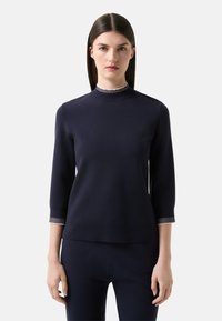 Marineblauer Pullover mit ribbeligem Stehkragen und Dreiviertelärmeln. Mit kontrastierenden gestreiften Bündchen. Glatte Stricktextur.