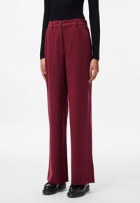 Burgundia laiad püksid, mis on valmistatud siledast kangast, varustatud nupusunaga, küljetaskute ja peene lõikega. Mustad jalanõud täiendavad ilmet.