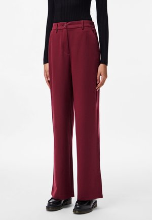 Pantalons larges bordeaux en tissu lisse, dotés d'une fermeture à bouton, de poches latérales et d'une coupe ajustée. Des chaussures noires viennent compléter le look.
