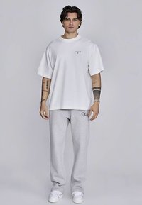 Wit T-shirt met korte mouwen en een subtiel logo, gecombineerd met grijze joggingbroek met een klein geborduurd detail, afgewerkt met witte sneakers.