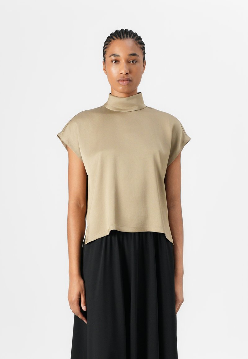 Top a maniche corte con collo alto in tessuto beige chiaro dalla texture liscia; vestibilità ampia, drappeggio sull'orlo, abbinato a una gonna nera.