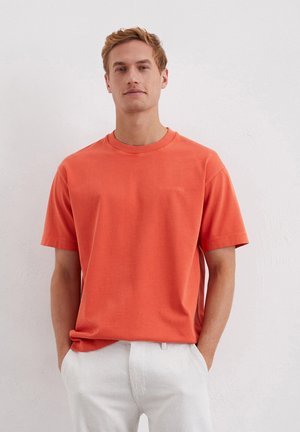 Short-sleeved coral crew neck t-shirt in cotton blend, featuring a subtle embroidered logo detail on the chest. Smooth texture and relaxed fit.