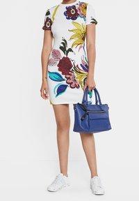 Robe courte à manches courtes à motifs floraux multicolores aux teintes vives ; associée à un sac à main bleu texturé et des baskets blanches.