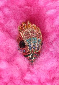 Kleurvolle ring bezet met edelstenen, gevormd als een schelp, met gouden metalen details en gezet in zacht roze materiaal.