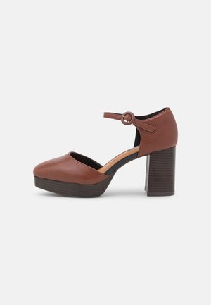 Chaussure Mary Jane à plateforme en cuir marron avec bride à boucle ronde à la cheville et talon bloc empilé sur fond blanc.