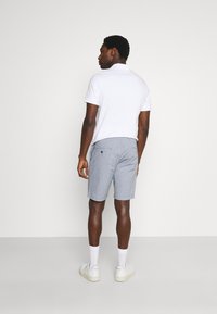 White polo shirt, grey check shorts, and white sneakers with ankle socks. Back view showcasing slim fit and pockets on shorts.