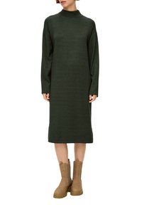 Ciemnozielona dzianinowa sukienka z wysokim kołnierzem, długimi rękawami i prostą sylwetką, zestawiona z brązowymi botkami do kostek z bocznymi akcentami.