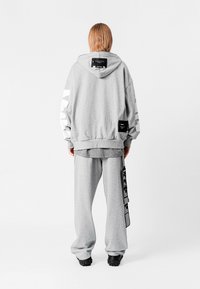 Sudadera gris de gran tamaño y pantalones de chándal a juego, fabricados en una mezcla de algodón. La sudadera presenta acentos blancos en las mangas y una etiqueta en la parte posterior.