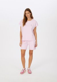 Light pink cotton t-shirt with short sleeves and a small graphic. Paired with matching pink shorts featuring two front pockets. Sneakers with pink accents.