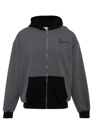 Pilkai zip-up džemperis su juoda kapuce ir kišenėmis. Minkšta medžiaga, susiraukšlėję rankogaliai ir apatinė dalis, ant krūtinės esantis mažas juodas logotipas.