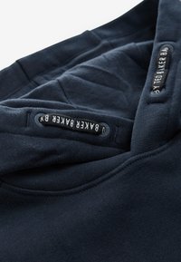 Mørkeblå sweatshirt med blød tekstur, med rund hals og mærkater med kontrasterende hvid tekst. Simpelt, funktionelt design.