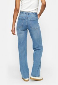 Kõrgelt talje sinised denim teksad, millel on lõdvestunud istuvus, sirged sääred ja kaks tagakotti. Kangas on pehme tekstuuriga ja kerge kulumisega.