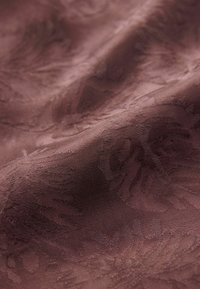 Tejido texturizado en marrón oscuro con sutiles patrones florales. Superficie suave y ligeramente brillante, creando una apariencia en capas.