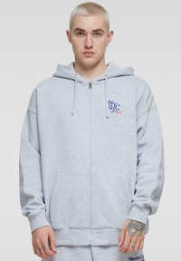 Grå zip-up hoodie med snøre i hætten, frontlommer og "NYC 93" broderet i blå og orange. Lavet af blødt bomuldsstof.