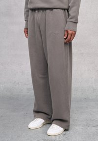 Grau Fleecepants mit elastischem Bund und Seitentaschen. Mit gesticktem Logo am Oberschenkel. Kombiniert mit weißen Sneakers.