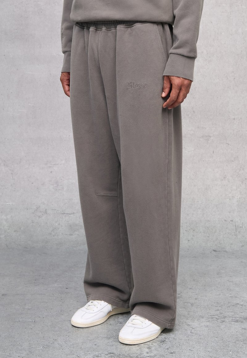 Grau Fleecepants mit elastischem Bund und Seitentaschen. Mit gesticktem Logo am Oberschenkel. Kombiniert mit weißen Sneakers.