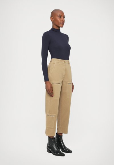 Top de culoare bleumarin cu guler înalt, asortat cu pantaloni cargo bej prevăzuți cu buzunare cu fermoar, completat de botine negre cu accente argintii.