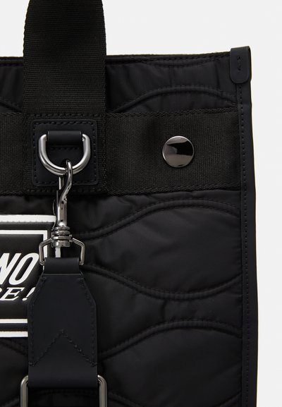 Borsa nera in nylon trapuntato con manico superiore piatto, accessori in metallo e strap regolabile. Presenta un patch decorativo con logo e una texture liscia.