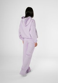 Felpa oversized lilla con cappuccio regolabile, abbinata a pantaloni della tuta larghi coordinati. Tessuto morbido e design semplice.