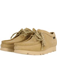Beige nubuk bőr casual cipők alacsony profilú dizájnnal, lekerekített orral, fűzős díszítéssel és texturált gumitalppal.