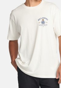 Hvit bomulls t-skjorte med rund hals, korte ermer og blå trykt design med "Billabong" og et emblem.