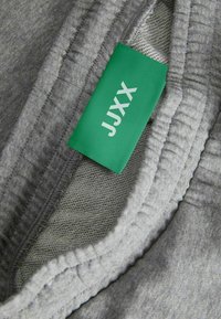 Grå klädfabric i olika texturer; inkluderar en grön tagg med texten "JXX" i vitt. Flera lager av tyget är synliga.